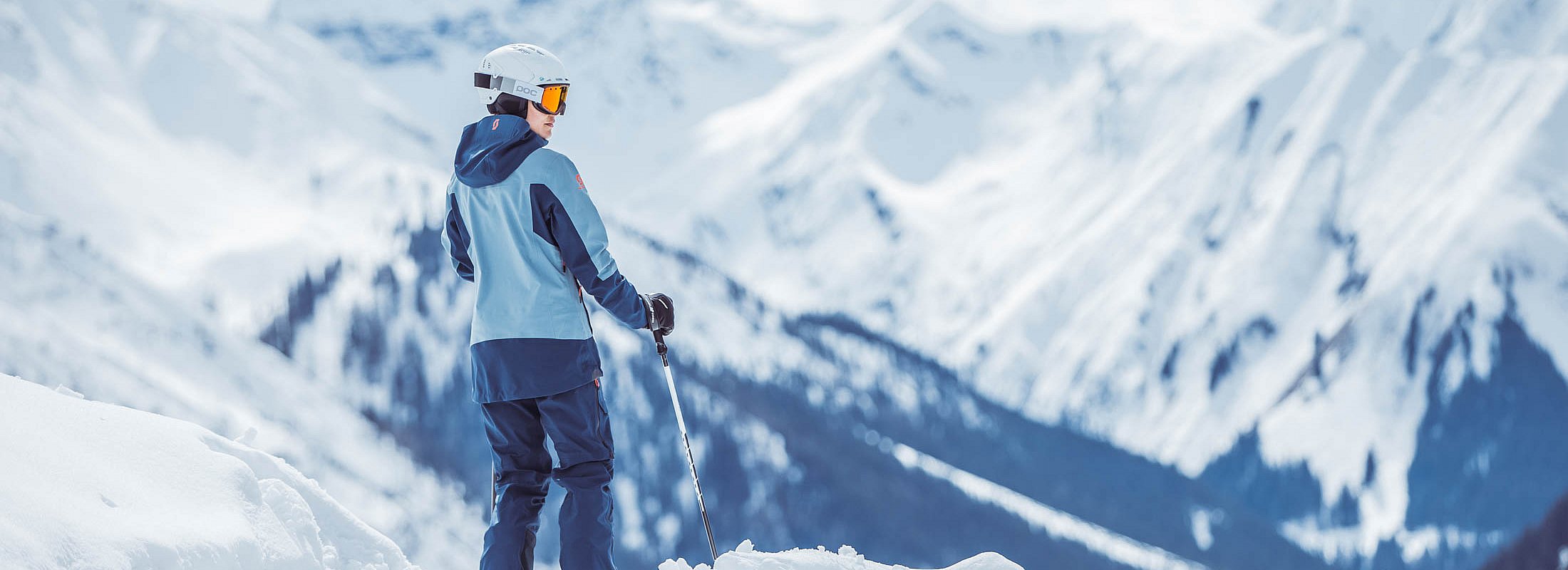 Skifahrer blickt über verschneite Alpenlandschaft mit Helm und Skistöcken